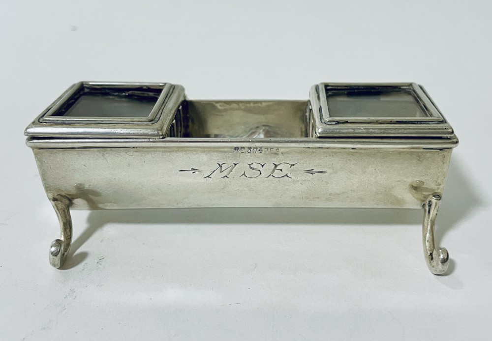 A rectangular Victorian silver double stamp trough with an engraved monogram, raised on four scrolled legs with two glass-topped compartments.