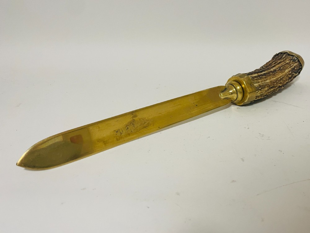 A Victorian desk set featuring a cut-glass inkwell in a brass frame, a brass letter opener with an antler handle, two small antler candlesticks, and a central brass-handled antler object. View X