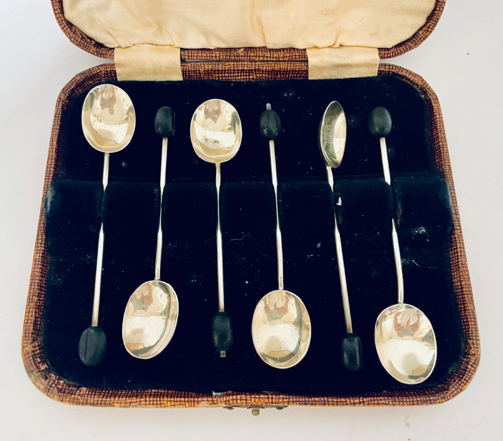 A set of six Art Deco silver coffee spoons with dark bean finials presented inside an open velvet-lined brown case. View II