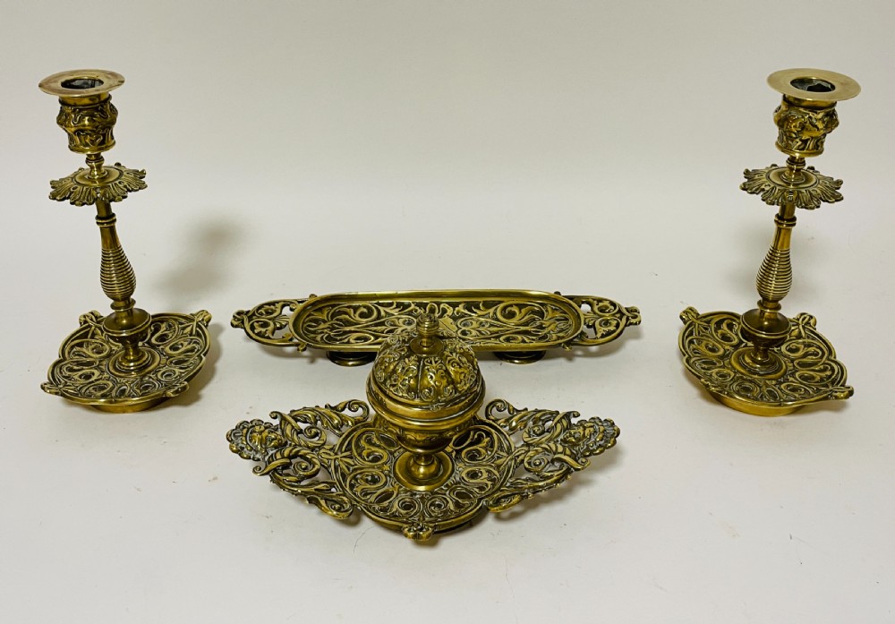 An ornate antique brass desk set featuring a lidded inkwell on a scrolled stand, a matching pen tray, and two turned brass candlesticks. View II