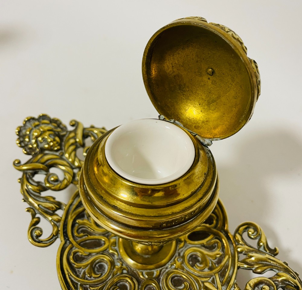 An ornate antique brass desk set featuring a lidded inkwell on a scrolled stand, a matching pen tray, and two turned brass candlesticks. View XI