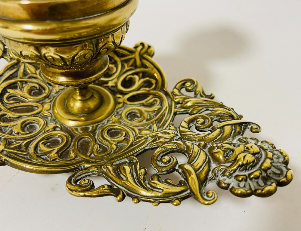 An ornate antique brass desk set featuring a lidded inkwell on a scrolled stand, a matching pen tray, and two turned brass candlesticks. View XII