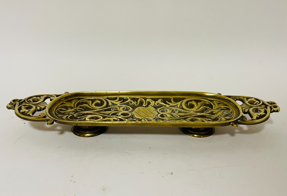 An ornate antique brass desk set featuring a lidded inkwell on a scrolled stand, a matching pen tray, and two turned brass candlesticks. View XVI