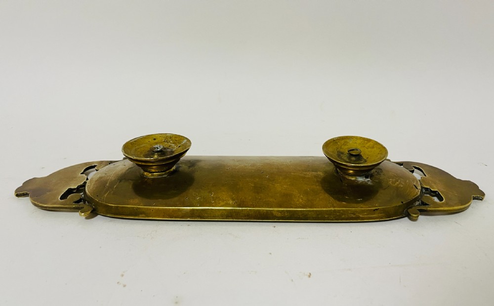 An ornate antique brass desk set featuring a lidded inkwell on a scrolled stand, a matching pen tray, and two turned brass candlesticks. View XIX