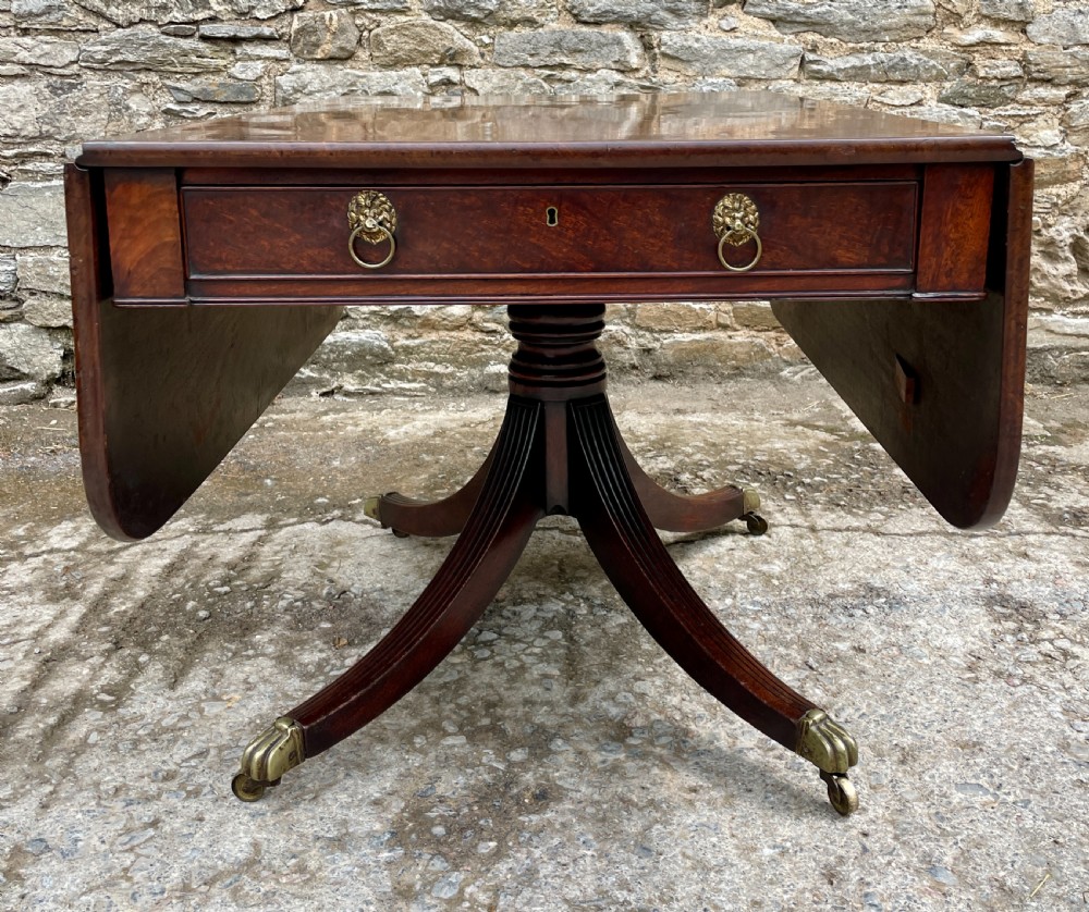 A Regency mahogany drop leaf pedestal table featuring reeded splayed legs, brass paw castors, and a drawer with lion mask handles. View V