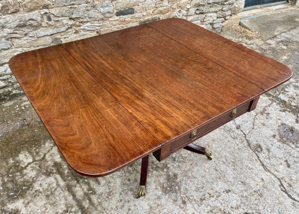 A Regency mahogany drop leaf pedestal table featuring reeded splayed legs, brass paw castors, and a drawer with lion mask handles. View VIII