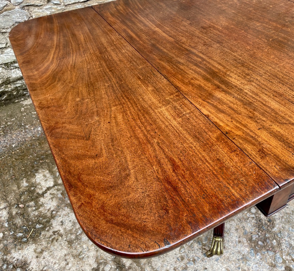 A Regency mahogany drop leaf pedestal table featuring reeded splayed legs, brass paw castors, and a drawer with lion mask handles. View IX