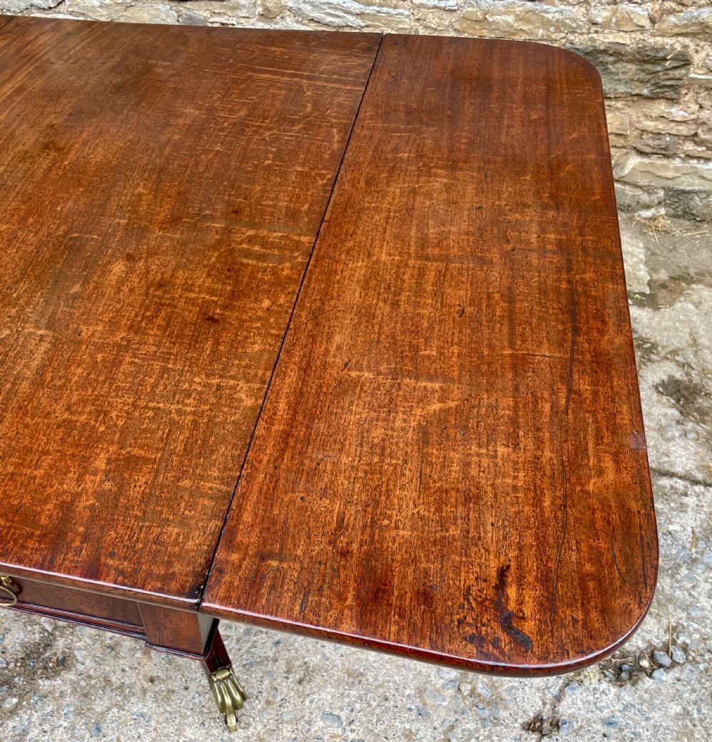 A Regency mahogany drop leaf pedestal table featuring reeded splayed legs, brass paw castors, and a drawer with lion mask handles. View XII