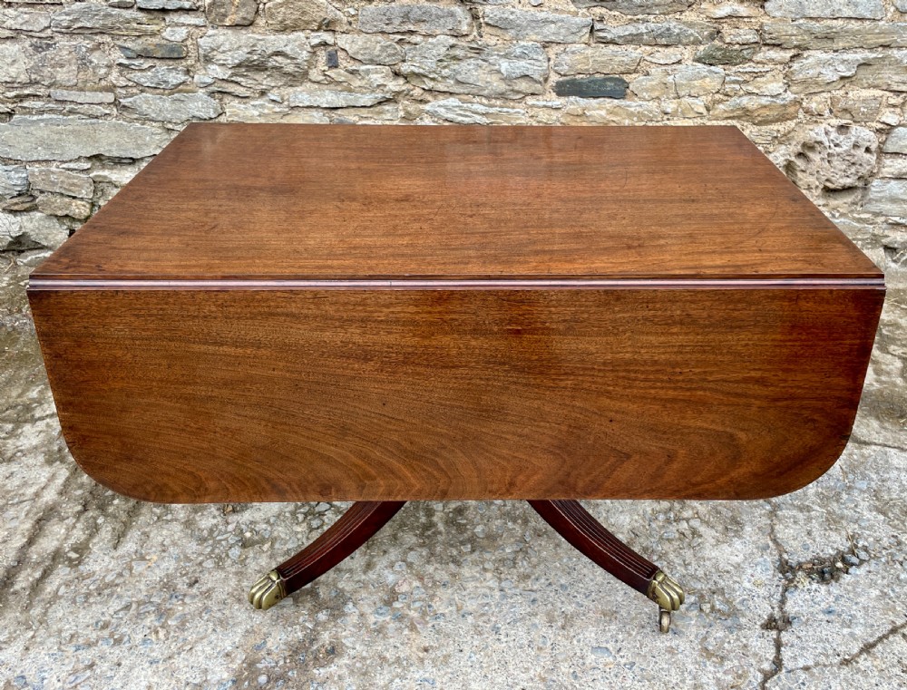 A Regency mahogany drop leaf pedestal table featuring reeded splayed legs, brass paw castors, and a drawer with lion mask handles. View XIV
