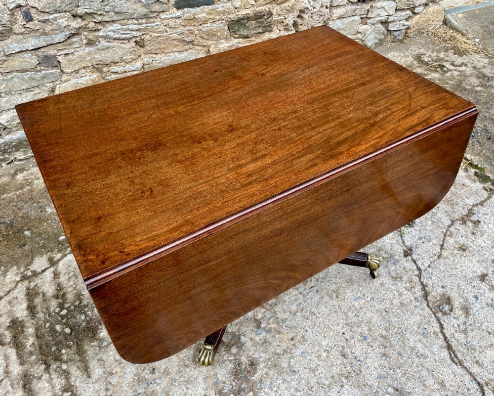 A Regency mahogany drop leaf pedestal table featuring reeded splayed legs, brass paw castors, and a drawer with lion mask handles. View XV