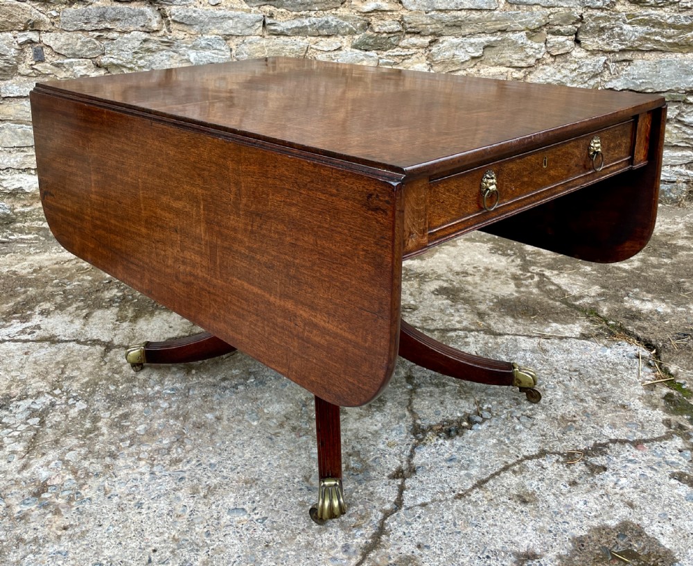 A Regency mahogany drop leaf pedestal table featuring reeded splayed legs, brass paw castors, and a drawer with lion mask handles. View XX