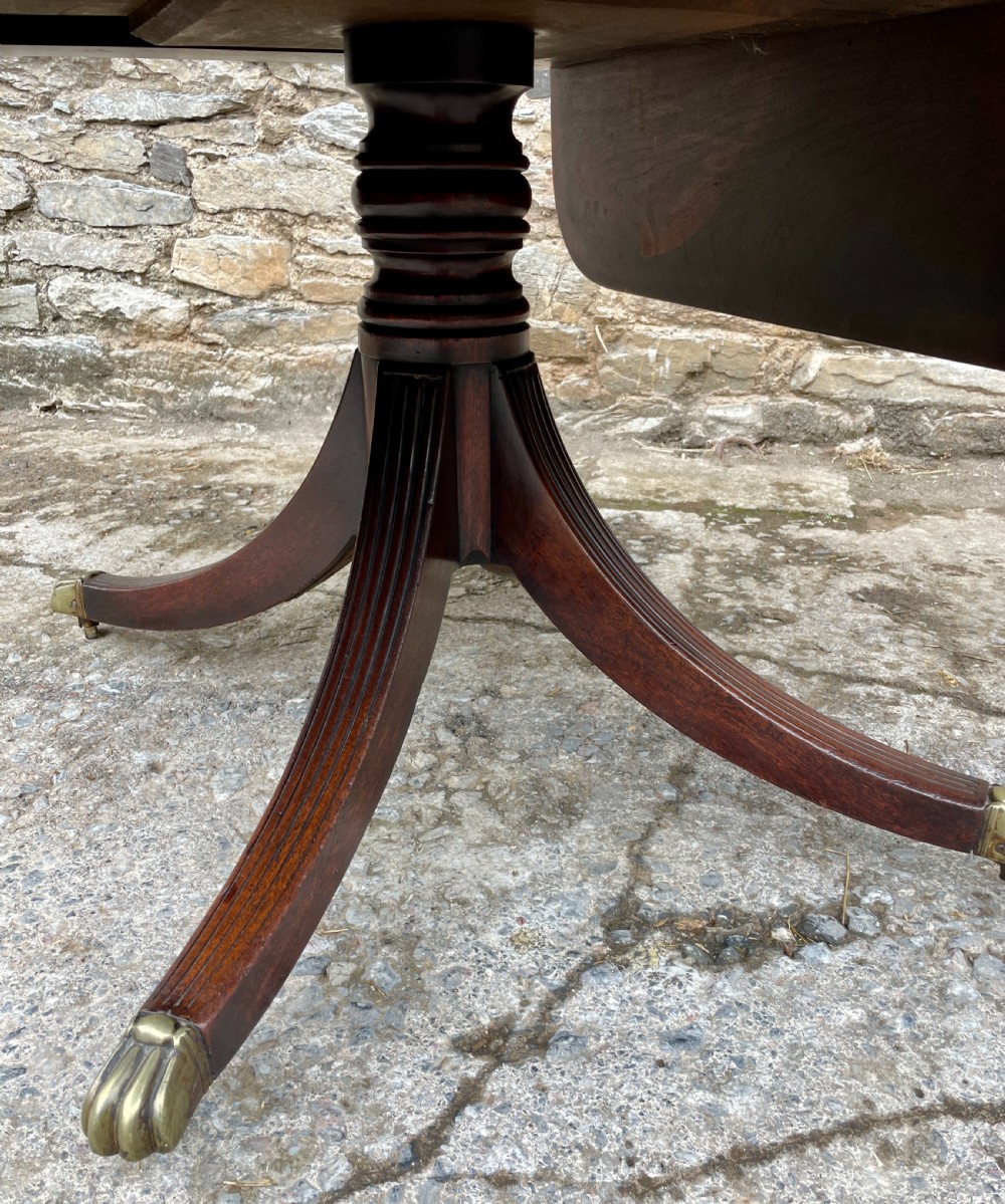 A Regency mahogany drop leaf pedestal table featuring reeded splayed legs, brass paw castors, and a drawer with lion mask handles. View XXI