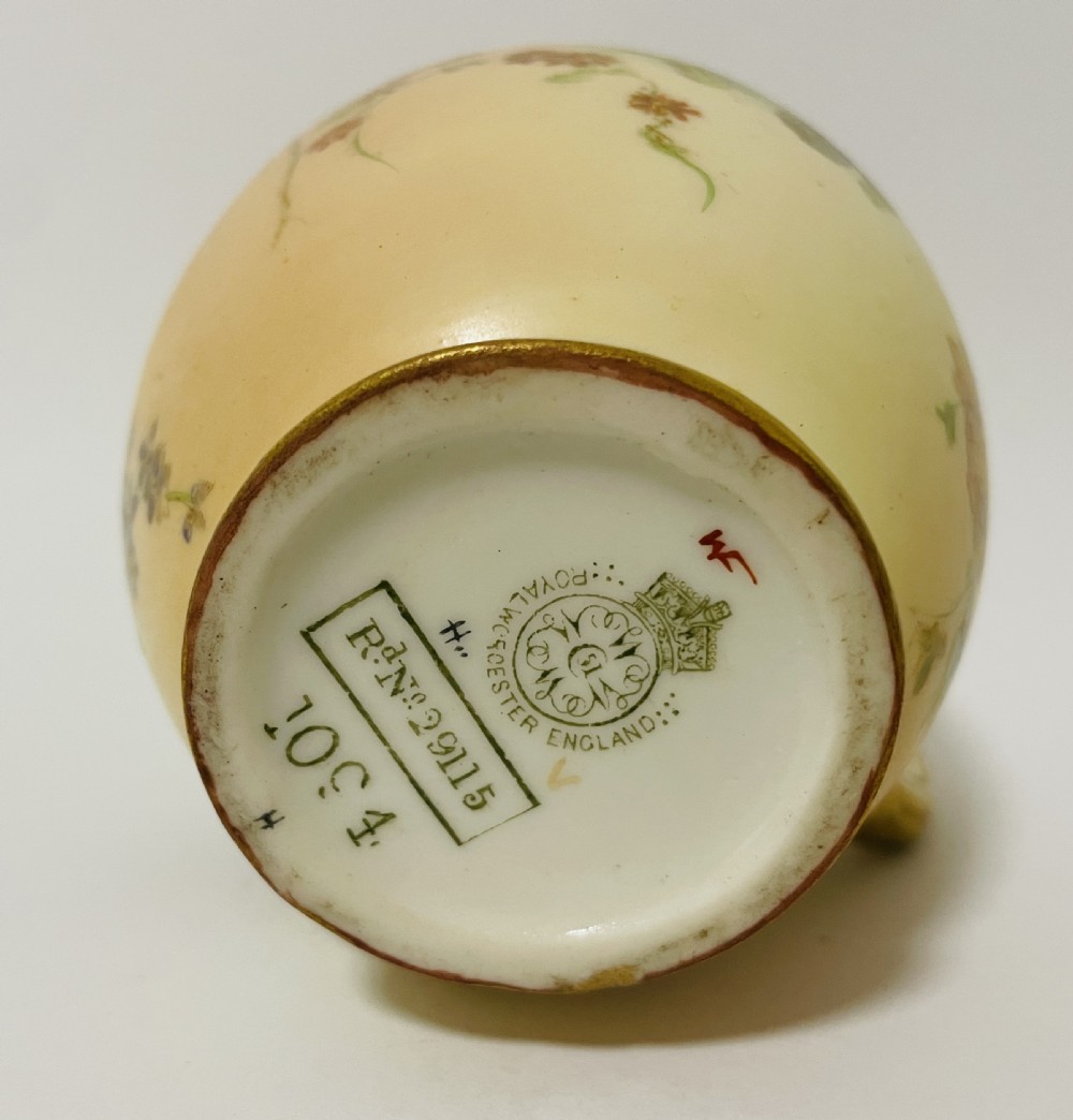 An Edwardian Royal Worcester porcelain jug featuring a blush cream body decorated with hand-painted yellow and pink flowers alongside a gilded handle and rim. View XI