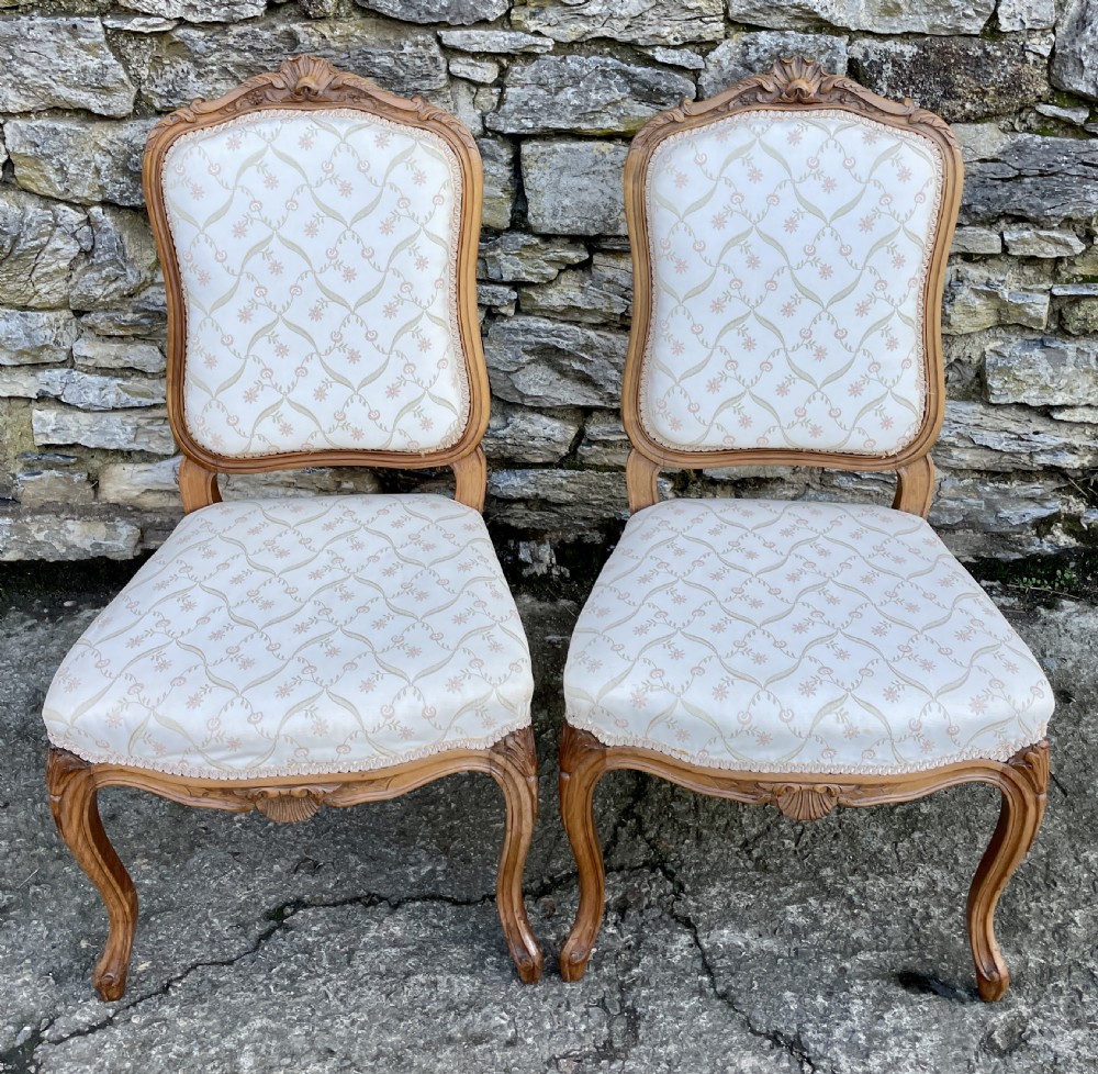 A pair of carved walnut French salon chairs featuring patterned cream upholstery, shell crest carvings, and cabriole legs.