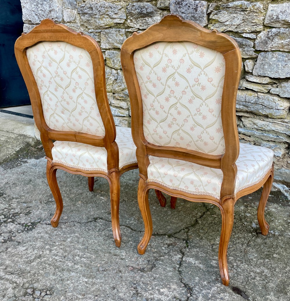 A pair of carved walnut French salon chairs featuring patterned cream upholstery, shell crest carvings, and cabriole legs. View V