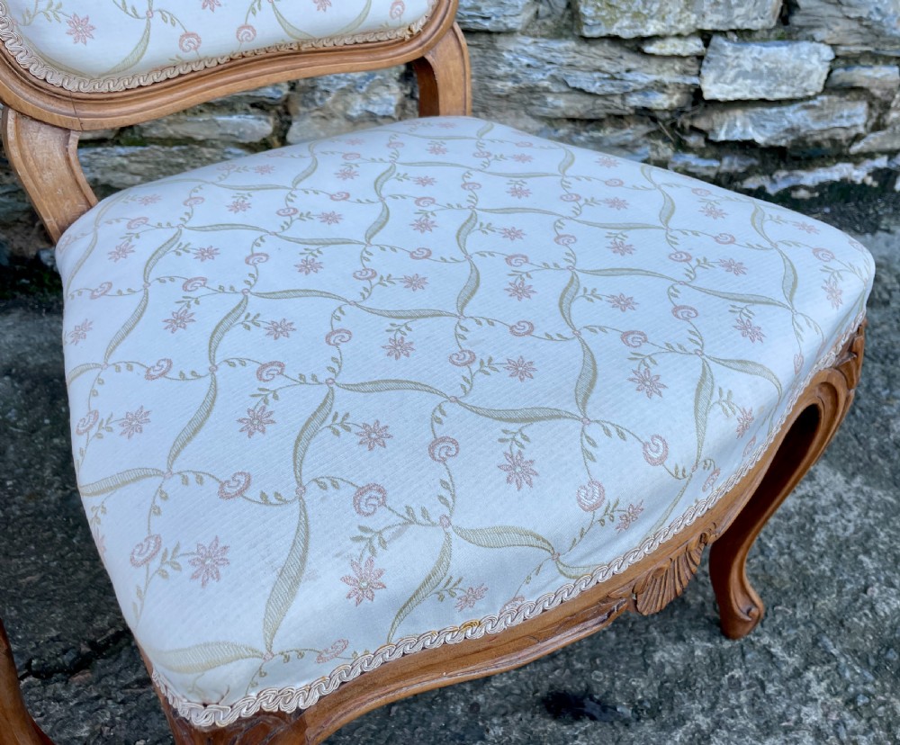 A pair of carved walnut French salon chairs featuring patterned cream upholstery, shell crest carvings, and cabriole legs. View VI