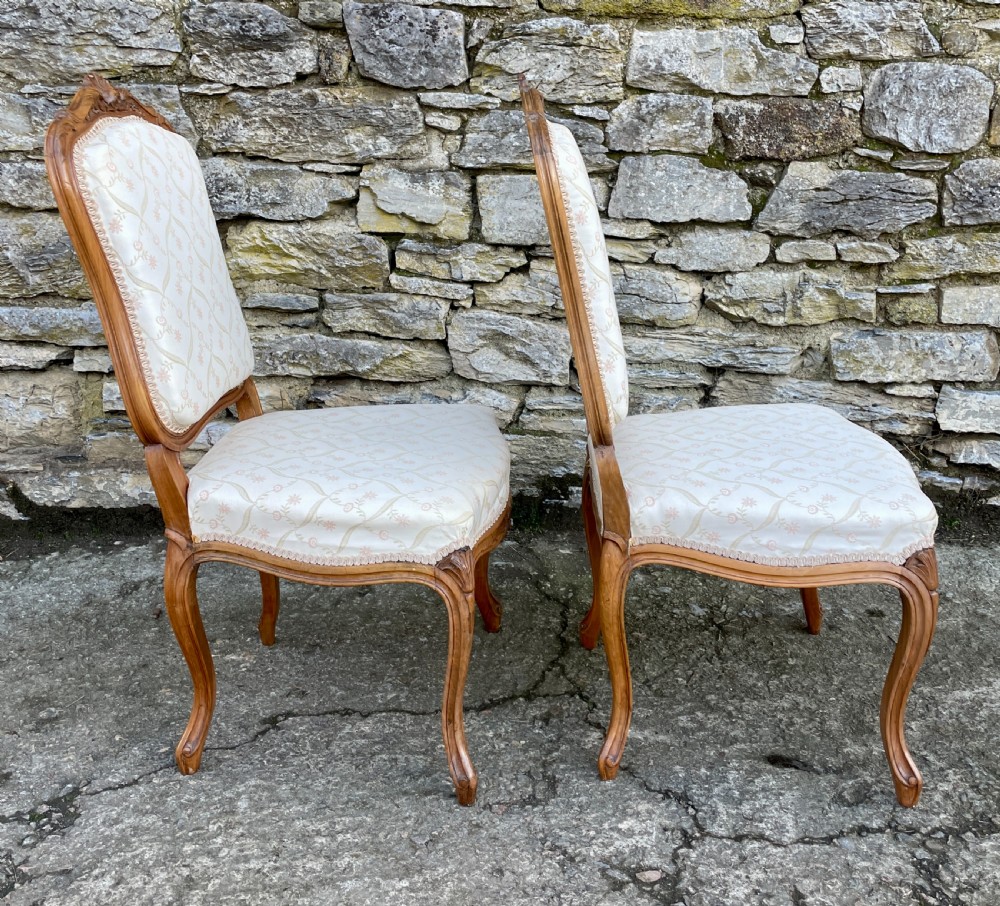 A pair of carved walnut French salon chairs featuring patterned cream upholstery, shell crest carvings, and cabriole legs. View VII
