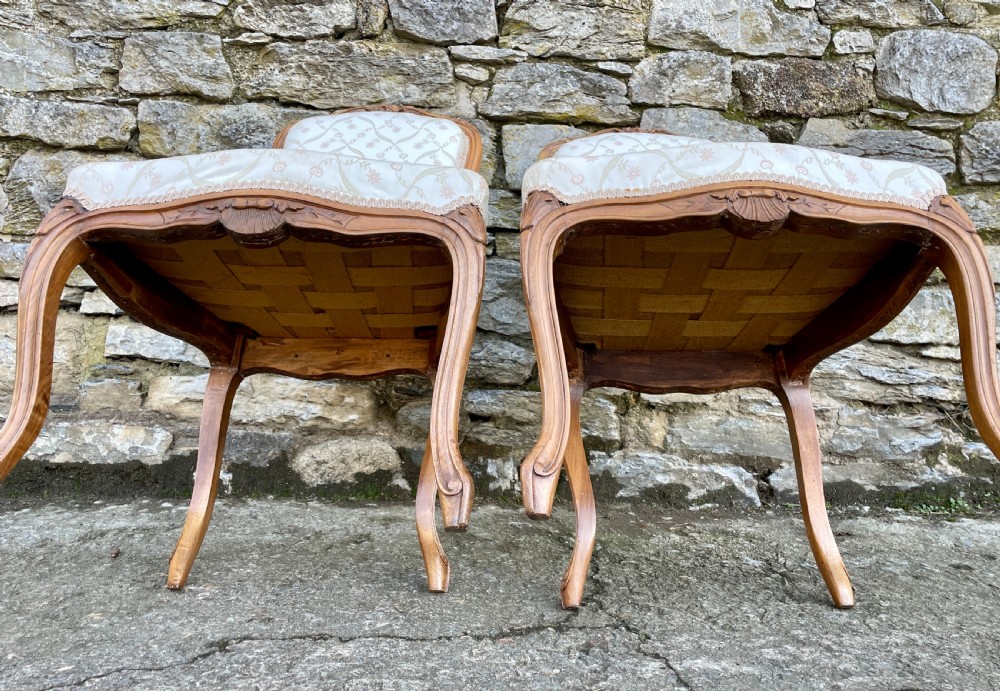 A pair of carved walnut French salon chairs featuring patterned cream upholstery, shell crest carvings, and cabriole legs. View X