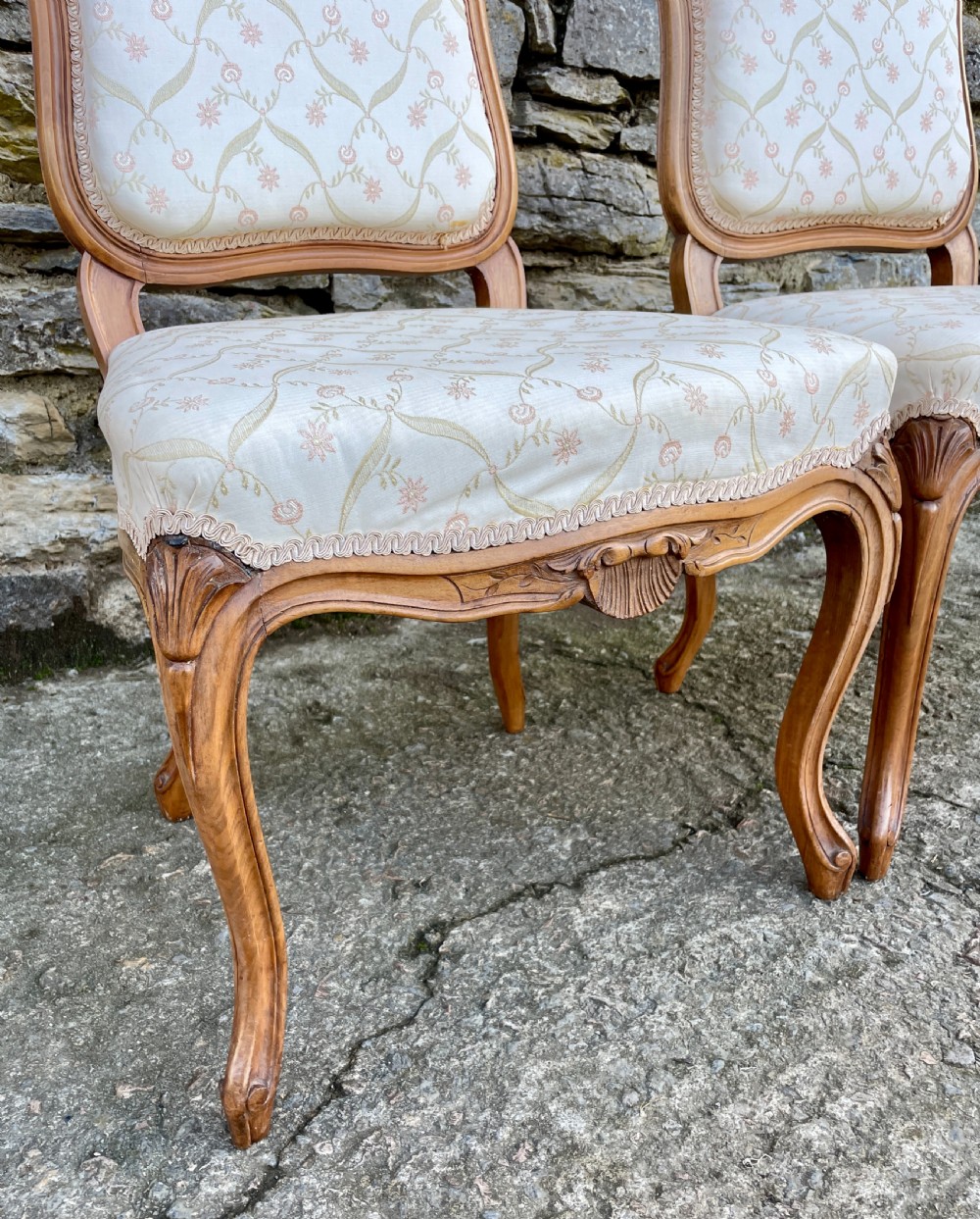 A pair of carved walnut French salon chairs featuring patterned cream upholstery, shell crest carvings, and cabriole legs. View XII