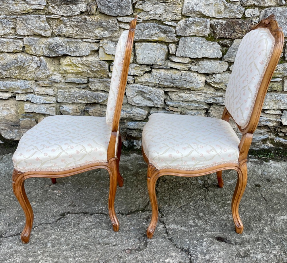 A pair of carved walnut French salon chairs featuring patterned cream upholstery, shell crest carvings, and cabriole legs. View XV