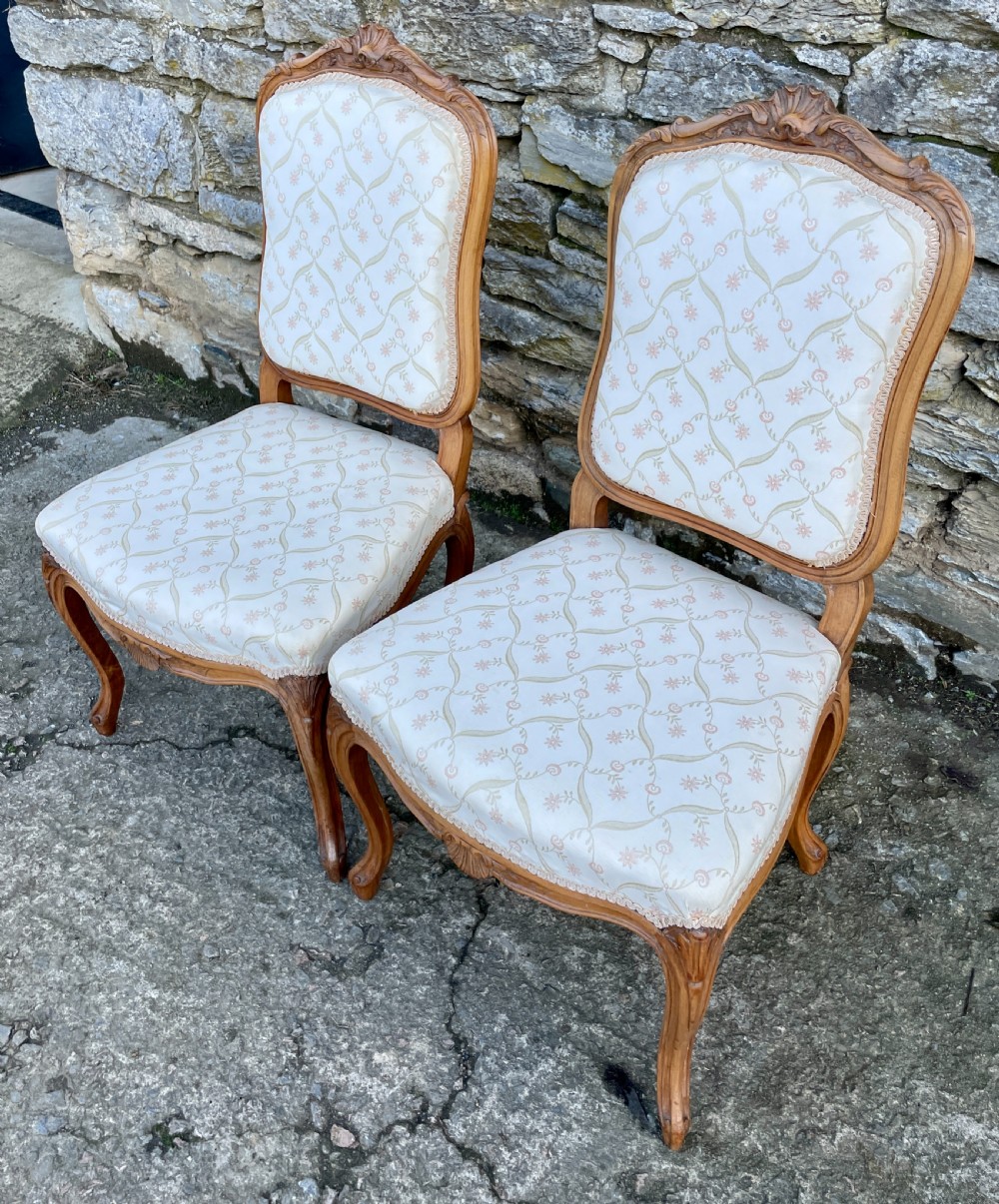 A pair of carved walnut French salon chairs featuring patterned cream upholstery, shell crest carvings, and cabriole legs. View XVI