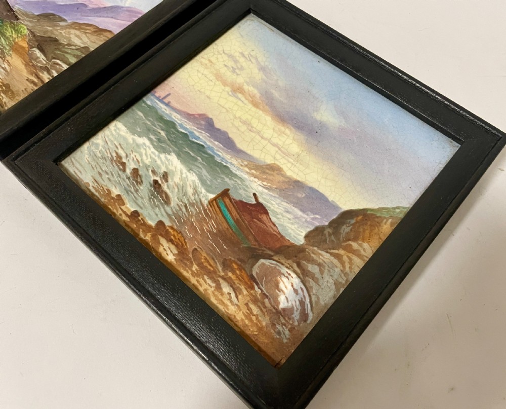 A pair of square Victorian ceramic tiles featuring hand-painted landscape scenes of a mountain river and a coastal shore, presented in dark wooden frames. View VIII