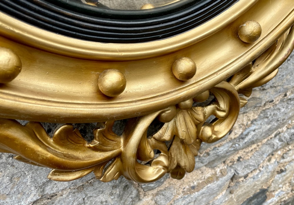 An ornate circular giltwood convex mirror featuring a carved eagle top cresting, acanthus leaf scrolling, ball mouldings, and an ebonised inner slip frame. View V
