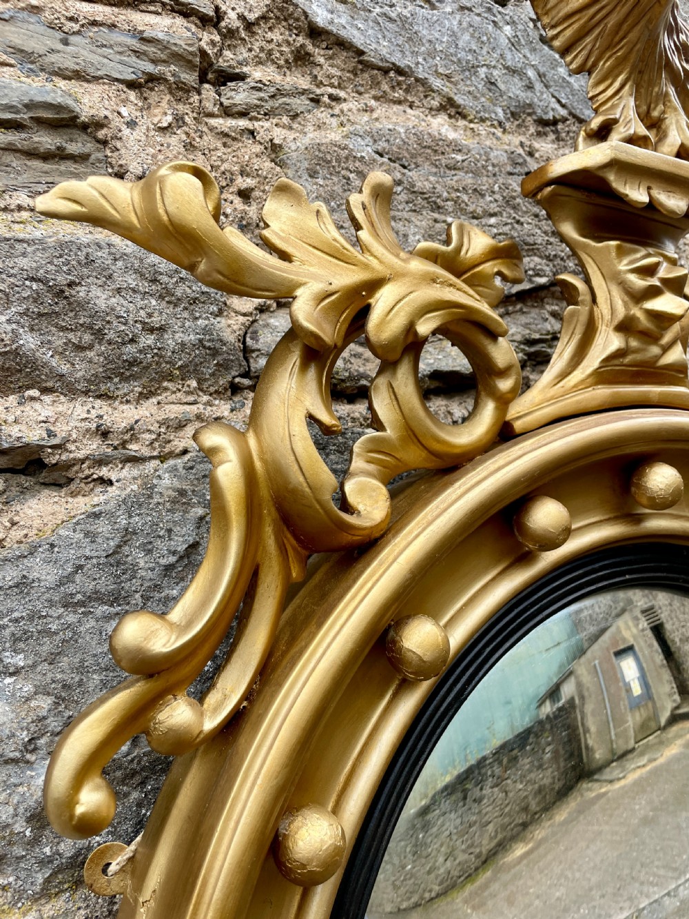 An ornate circular giltwood convex mirror featuring a carved eagle top cresting, acanthus leaf scrolling, ball mouldings, and an ebonised inner slip frame. View VII