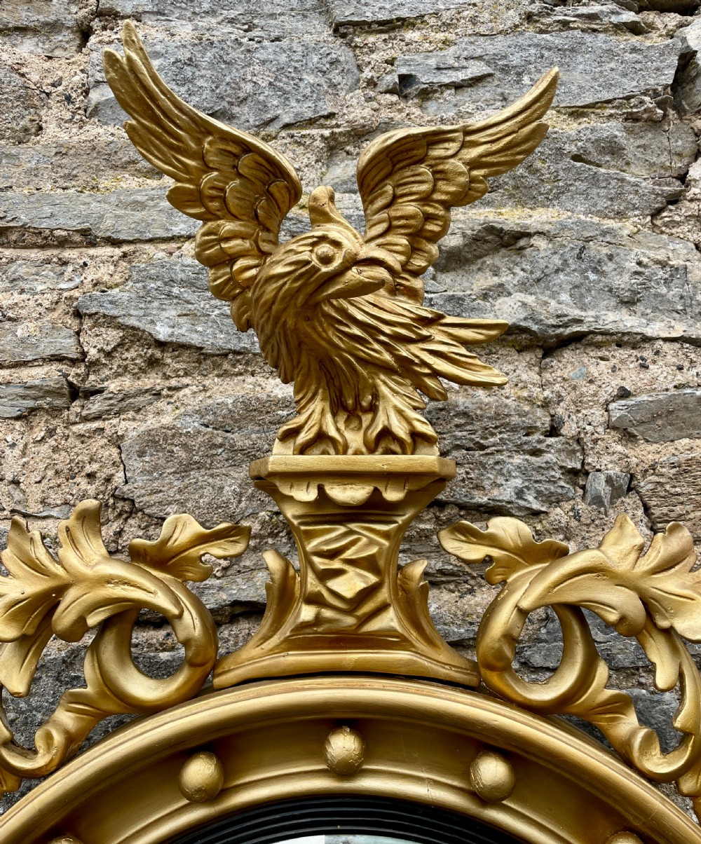 An ornate circular giltwood convex mirror featuring a carved eagle top cresting, acanthus leaf scrolling, ball mouldings, and an ebonised inner slip frame. View IX