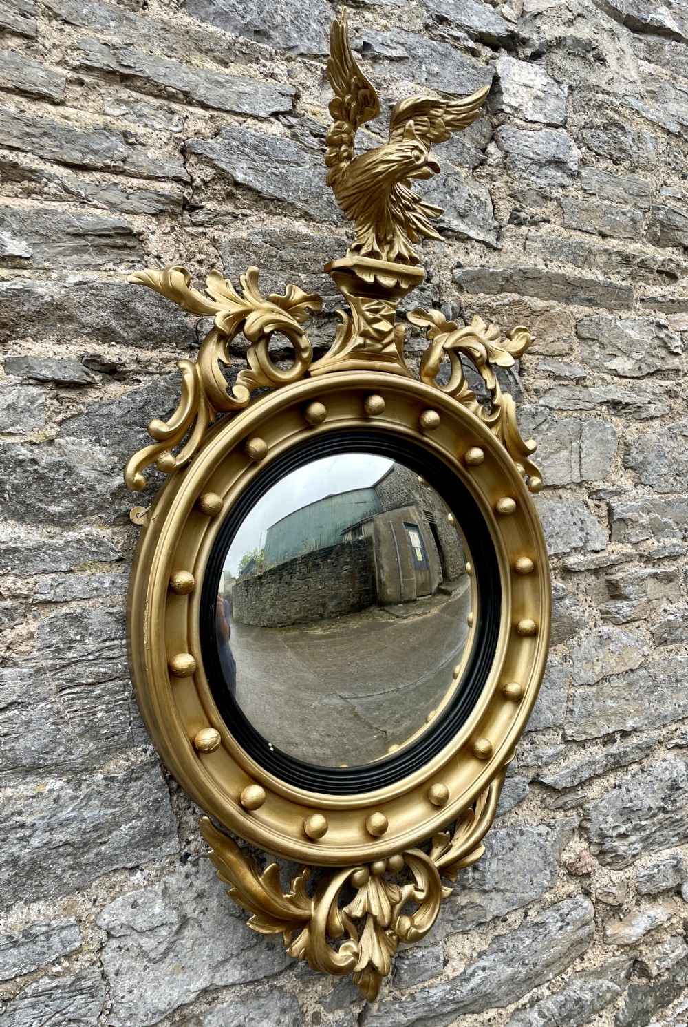 An ornate circular giltwood convex mirror featuring a carved eagle top cresting, acanthus leaf scrolling, ball mouldings, and an ebonised inner slip frame. View XVI