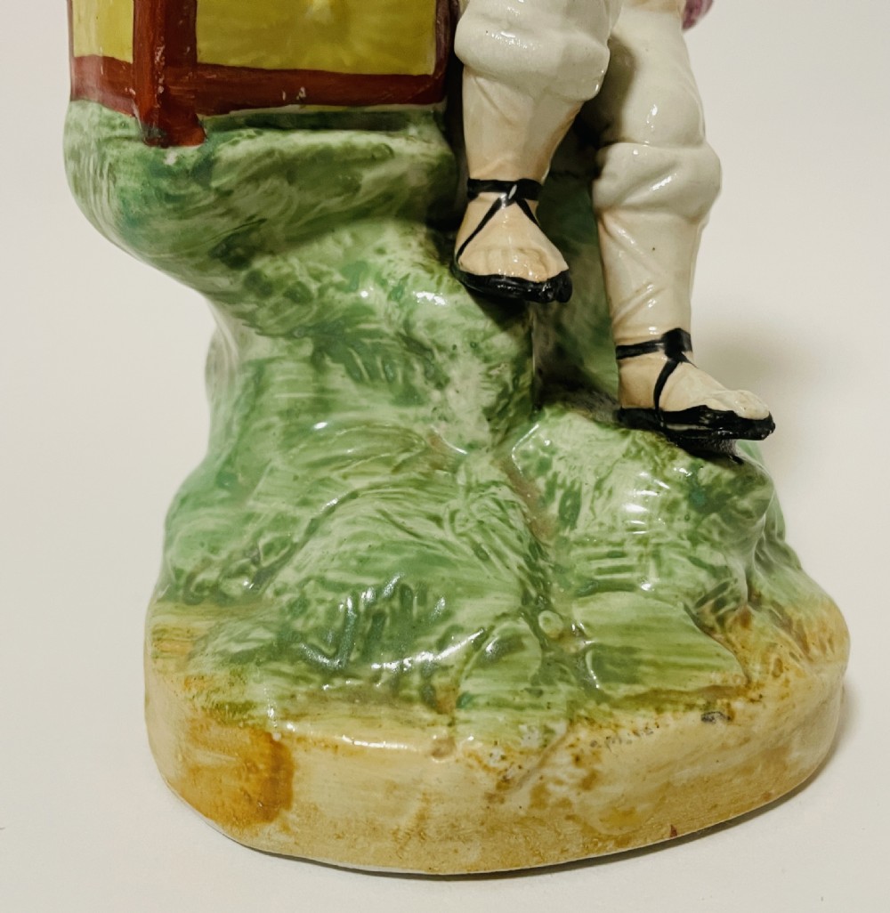 A Victorian Staffordshire earthenware figure depicting a seated boy in a straw hat and pink jacket alongside a monkey resting on a small brown chest. View XI