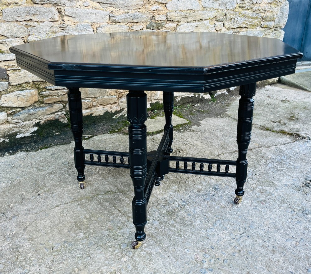 An octagonal ebonised Aesthetic Movement centre table featuring turned legs, brass castors, and a spindle X-frame stretcher. View III