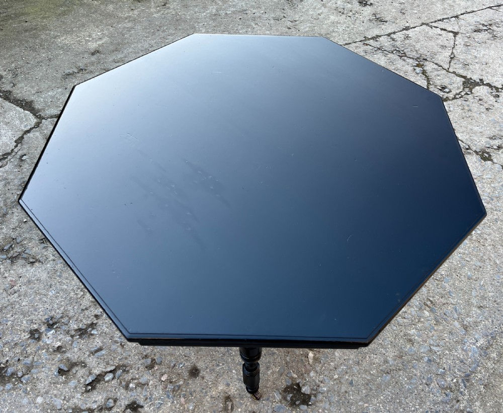 An octagonal ebonised Aesthetic Movement centre table featuring turned legs, brass castors, and a spindle X-frame stretcher. View VI
