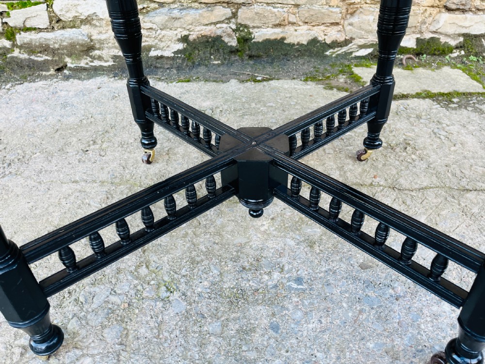 An octagonal ebonised Aesthetic Movement centre table featuring turned legs, brass castors, and a spindle X-frame stretcher. View VIII