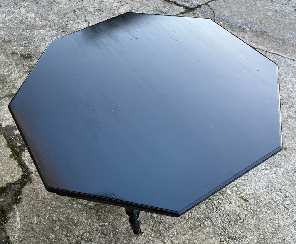 An octagonal ebonised Aesthetic Movement centre table featuring turned legs, brass castors, and a spindle X-frame stretcher. View X