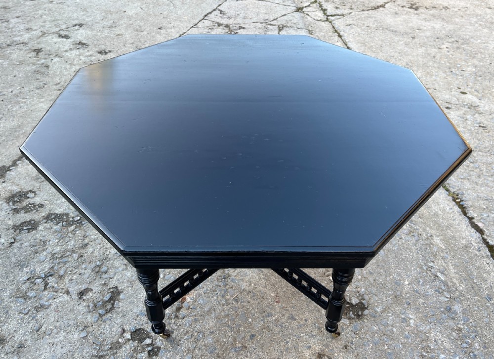 An octagonal ebonised Aesthetic Movement centre table featuring turned legs, brass castors, and a spindle X-frame stretcher. View XII