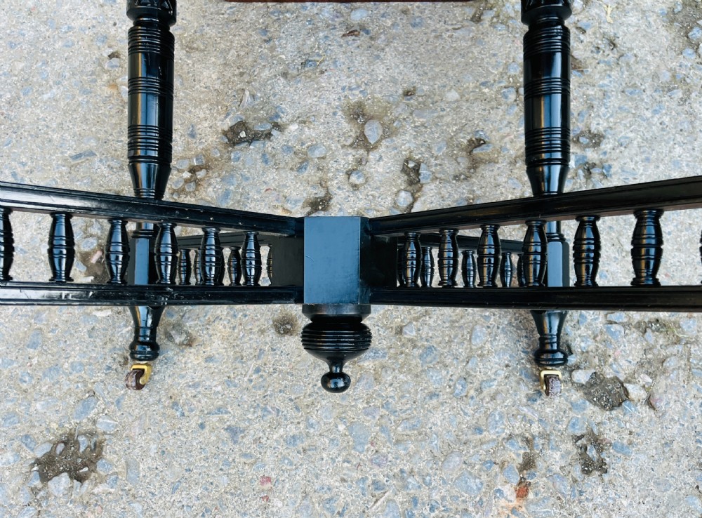 An octagonal ebonised Aesthetic Movement centre table featuring turned legs, brass castors, and a spindle X-frame stretcher. View XV