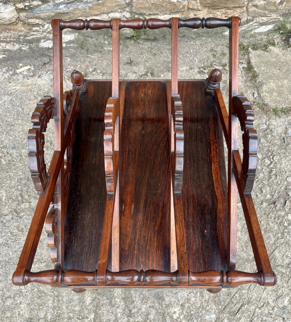 A Regency rosewood music canterbury featuring carved wreath motif side panels, slatted partitions, a single base drawer, and turned legs on brass castors. View VIII