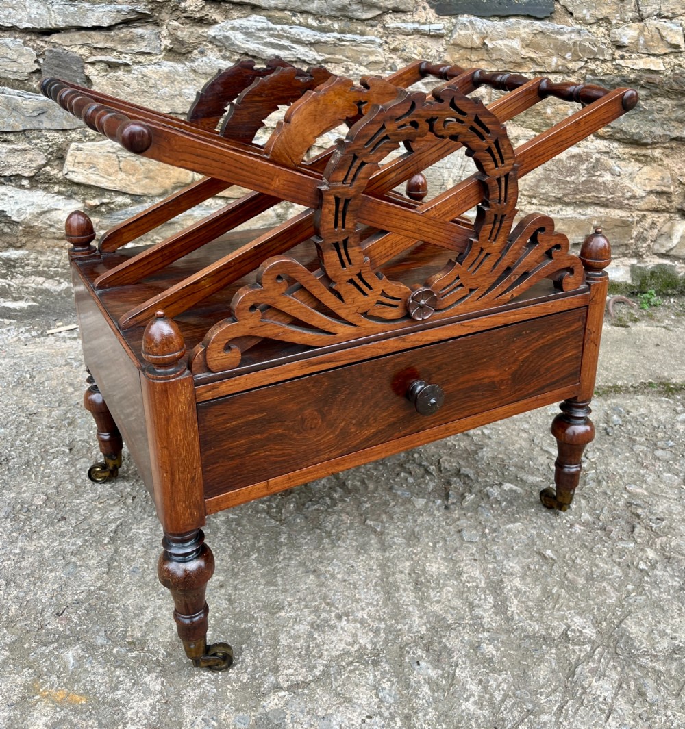 A Regency rosewood music canterbury featuring carved wreath motif side panels, slatted partitions, a single base drawer, and turned legs on brass castors. View XI