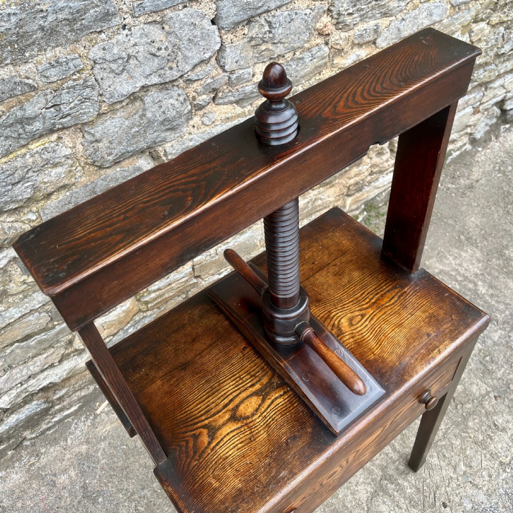 An antique oak and elm book press table featuring a central turned wooden screw mechanism above a single drawer with two round knobs. View X