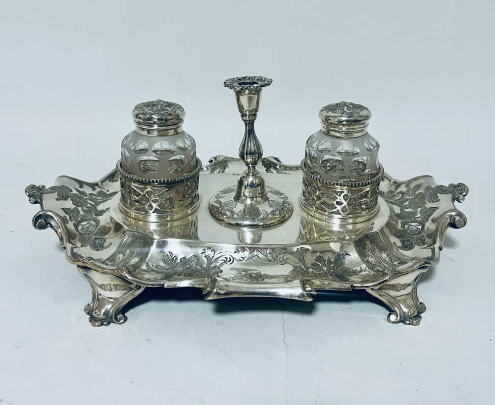 A Victorian silver-plated inkstand featuring an ornate tray with scrolled feet, two cut-glass inkwells in pierced holders, and a central taperstick.