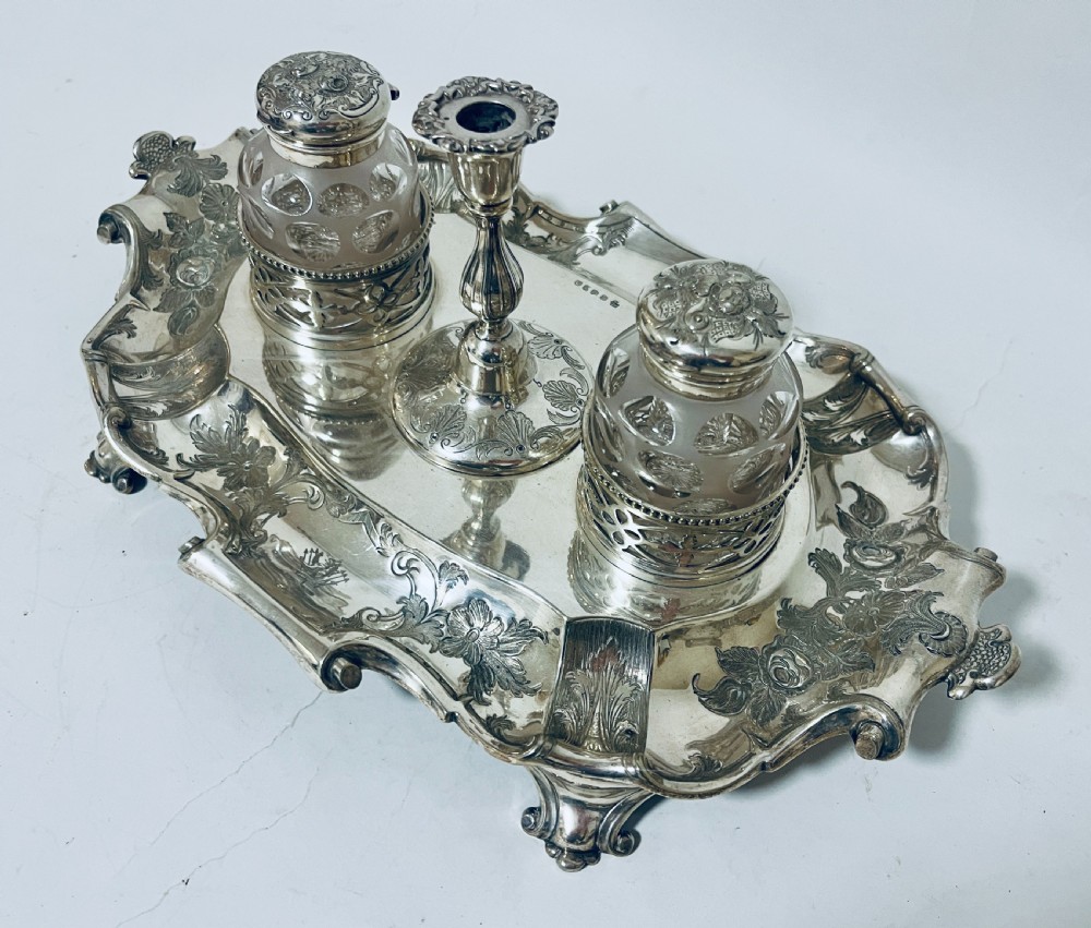 A Victorian silver-plated inkstand featuring an ornate tray with scrolled feet, two cut-glass inkwells in pierced holders, and a central taperstick. View II