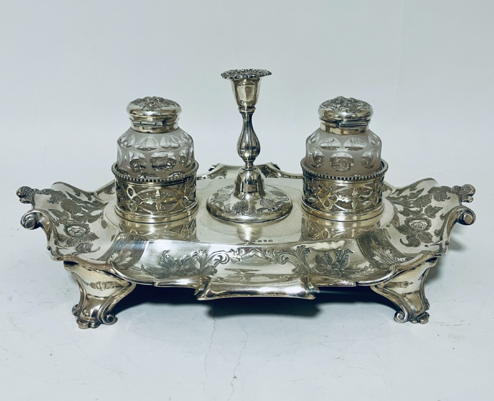 A Victorian silver-plated inkstand featuring an ornate tray with scrolled feet, two cut-glass inkwells in pierced holders, and a central taperstick. View VI