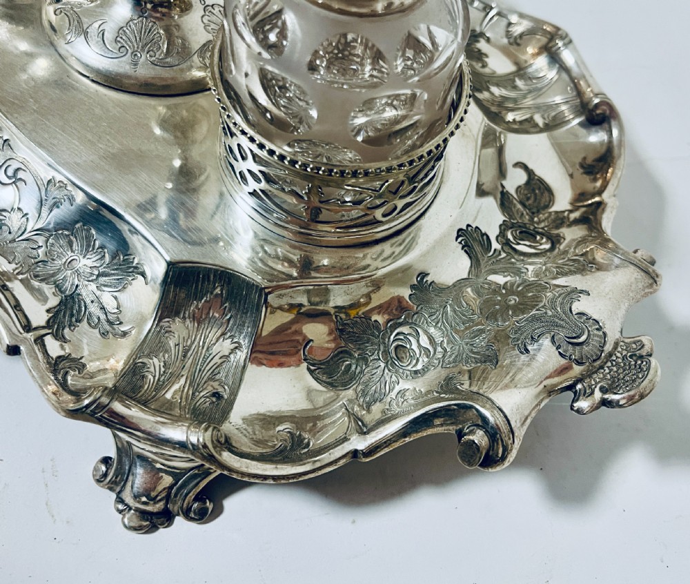 A Victorian silver-plated inkstand featuring an ornate tray with scrolled feet, two cut-glass inkwells in pierced holders, and a central taperstick. View VII