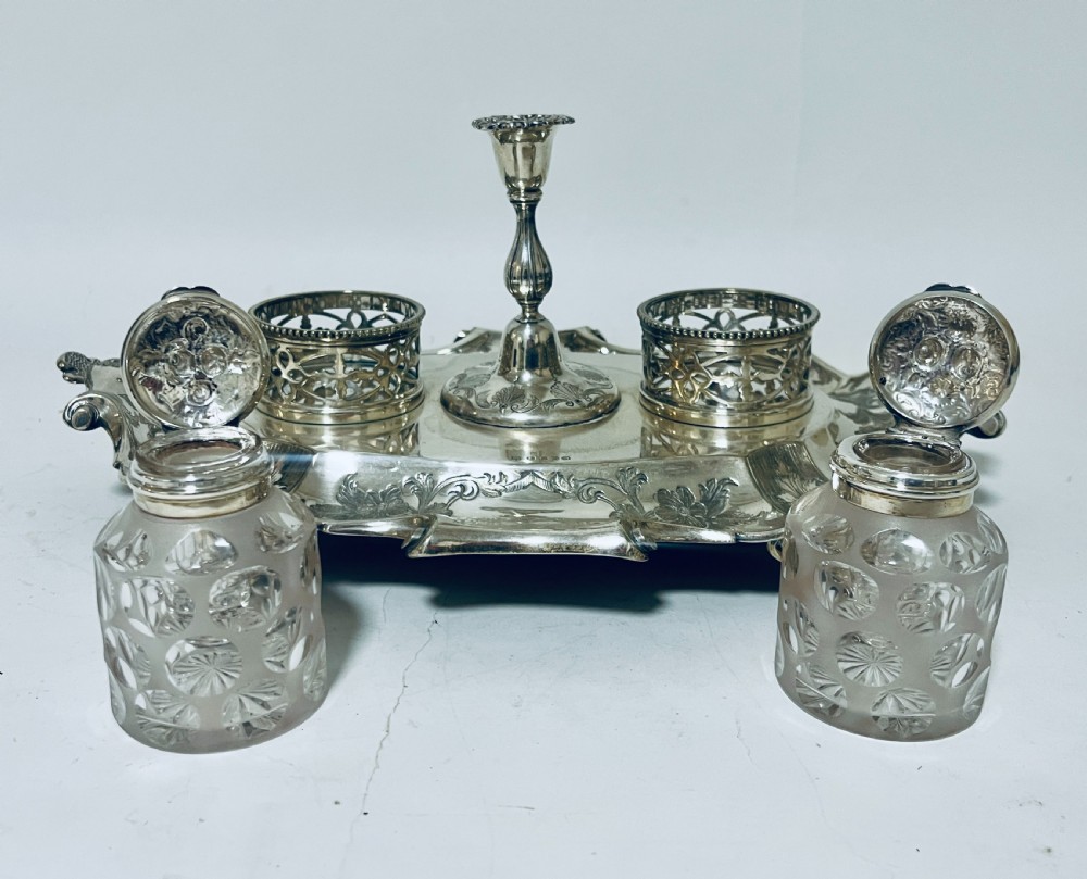 A Victorian silver-plated inkstand featuring an ornate tray with scrolled feet, two cut-glass inkwells in pierced holders, and a central taperstick. View VIII