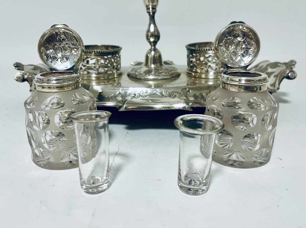 A Victorian silver-plated inkstand featuring an ornate tray with scrolled feet, two cut-glass inkwells in pierced holders, and a central taperstick. View IX