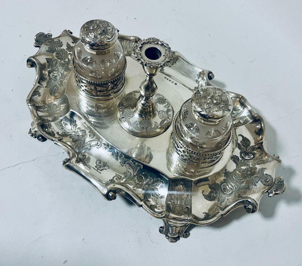 A Victorian silver-plated inkstand featuring an ornate tray with scrolled feet, two cut-glass inkwells in pierced holders, and a central taperstick. View X