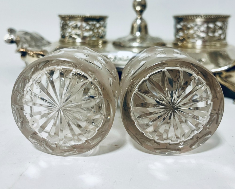 A Victorian silver-plated inkstand featuring an ornate tray with scrolled feet, two cut-glass inkwells in pierced holders, and a central taperstick. View XI