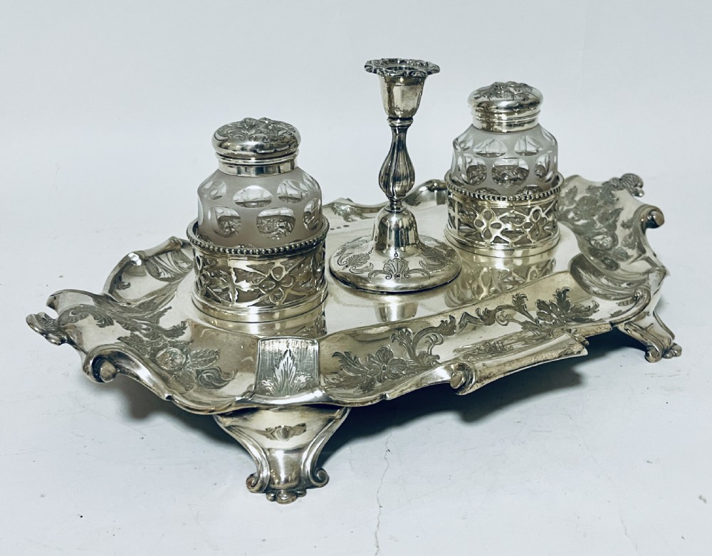 A Victorian silver-plated inkstand featuring an ornate tray with scrolled feet, two cut-glass inkwells in pierced holders, and a central taperstick. View XIII