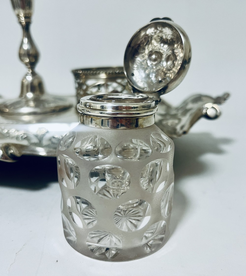 A Victorian silver-plated inkstand featuring an ornate tray with scrolled feet, two cut-glass inkwells in pierced holders, and a central taperstick. View XIV